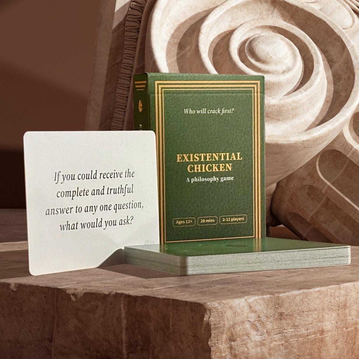 The Existential Chicken box and deck beside a question card on carved stone